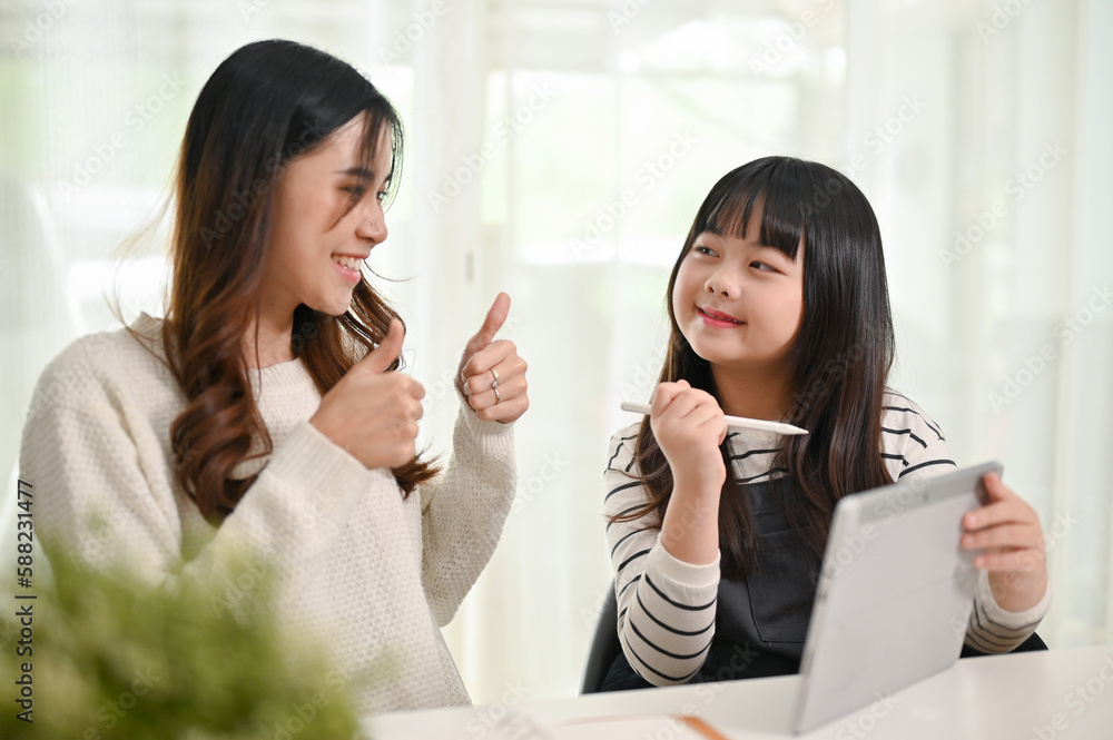 Cheerful Asian mom and her daughter spending time together at home, using tablet Cheerful Asian mom and her daughter spending time together at home, using tablet