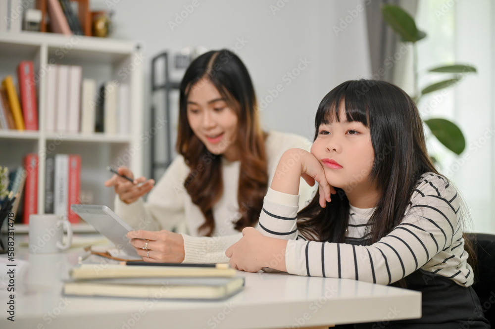 Lazy and bored young Asian girl sits at a table with her hand on her chin, too tired to study Lazy and bored young Asian girl sits at a table with her hand on her chin, too tired to study