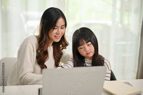 Kind and caring Asian sister helping her little sister with homework at home.