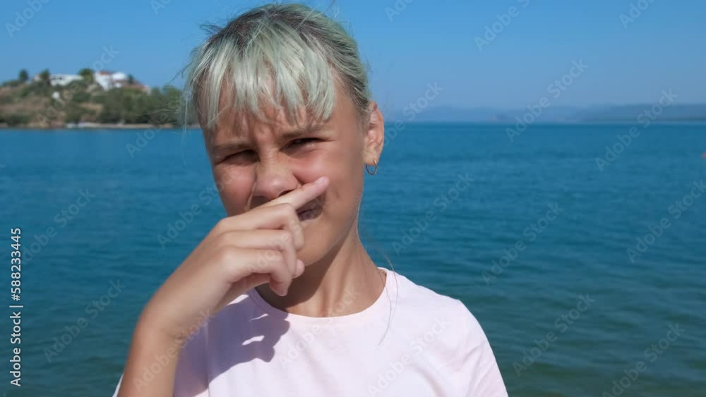 Seasonal allergies. The girl rubs her nose and sneezes on the background of the blue sea.
