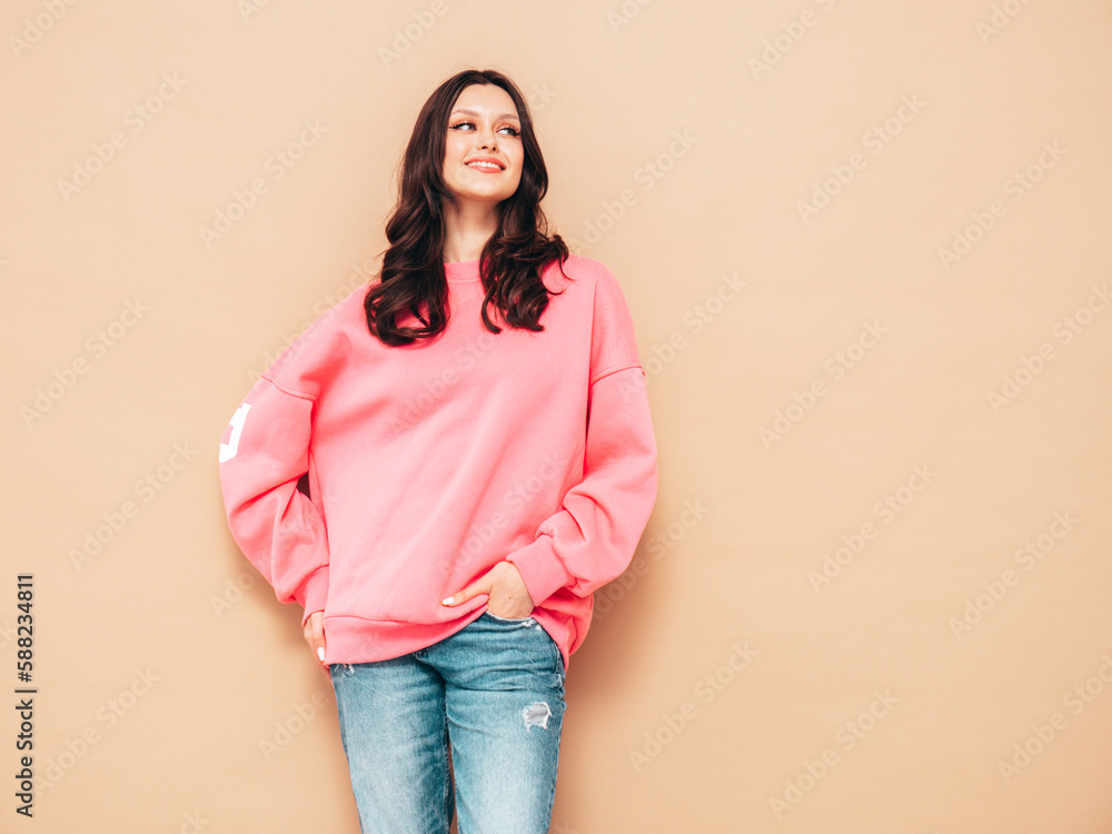 Young beautiful smiling female in trendy summer jeans and pink sweater clothes. Sexy carefree woman posing near beige wall in studio. Positive model. Cheerful and happy Young beautiful smiling female in trendy summer jeans and pink sweater clothes. Sexy carefree woman posing near beige wall in studio. Positive model. Cheerful and happy