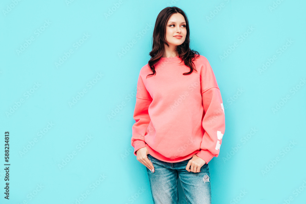 Young beautiful smiling female in trendy summer jeans and pink sweater clothes. Sexy carefree woman isolated on blue wall in studio. Positive model having fun. Cheerful and happy Young beautiful smiling female in trendy summer jeans and pink sweater clothes. Sexy carefree woman isolated on blue wall in studio. Positive model having fun. Cheerful and happy