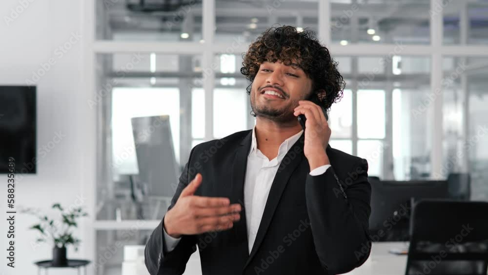 Happy Indian business person entering a phone number on his mobile phone and talking to business partner in office environment. Man is making an important business call or perhaps arranging meeting. Happy Indian business person entering a phone number on his mobile phone and talking to business partner in office environment. Man is making an important business call or perhaps arranging meeting.