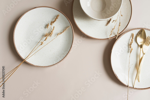 beige empty porcelain plate on pastel background with golden cutlery and dried flowers. Boho minimalist aesthetic. Dishware mock up.