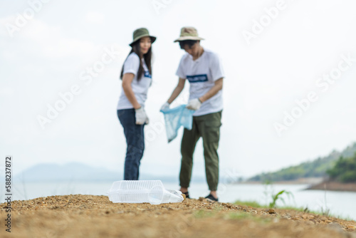 Close up Garbage plastic with blur male and female volunteers background, conducting environmental cooperation, saving world reducing global warming, Clean plastic bag waste in natural attractions.