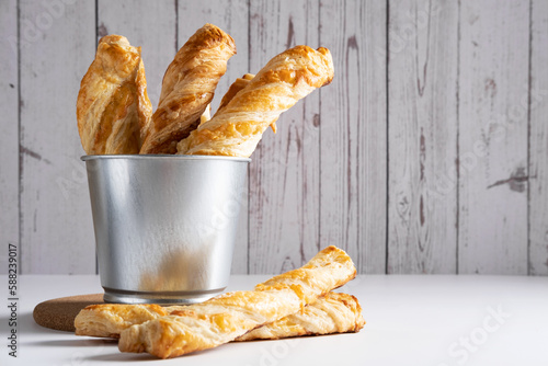 Puff pastry cheese sticks in a metal bucket on a light background