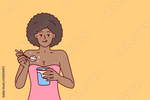 African American woman eating ice cream enjoying cold dessert to cool down after hot walk. Curly ethnic girl with ice cream satisfies hunger and licks lips wanting to be refreshed in summer weather 