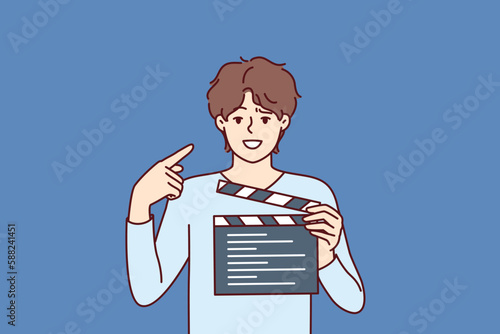 Man producer with clapboard in hands looks at screen while working on set of film or clip with Hollywood actors. Guy director or producer points finger at face, recommending staff of set to smile 