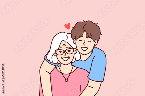 Noble guy teenager hugging elderly grandmother showing love and care for ancestors and communicating with family. Happy retired woman near caring son spending time in family atmosphere 