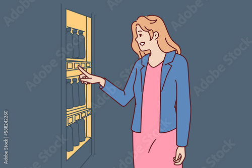 Woman stands near vending machine choosing snack or drink to buy and satisfy hunger and thirst. Young happy girl wishes to buy soda or sandwich in vending machine or automated store 