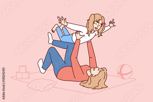 Caring mother lying on floor lifts laughing daughter enjoying playing with child on long-awaited day off. Carefree Caucasian family from mom self raising daughter or babysitting woman