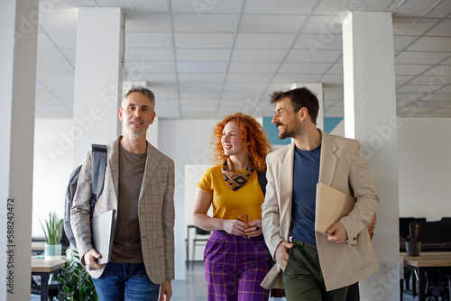 Coworkers talking while walking through corridor at office 