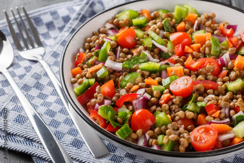 Fresh lentil salad with summer vegetables close-up in a plate on a wooden table. Horizontal
