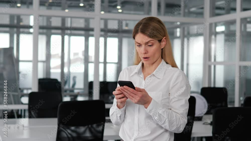 European woman in office holding smartphone, upset by receiving terrible news via SMS. Negative emotions and frustration due to a damaged device, lost internet connection, or a need for gadget repair. European woman in office holding smartphone, upset by receiving terrible news via SMS. Negative emotions and frustration due to a damaged device, lost internet connection, or a need for gadget repair.