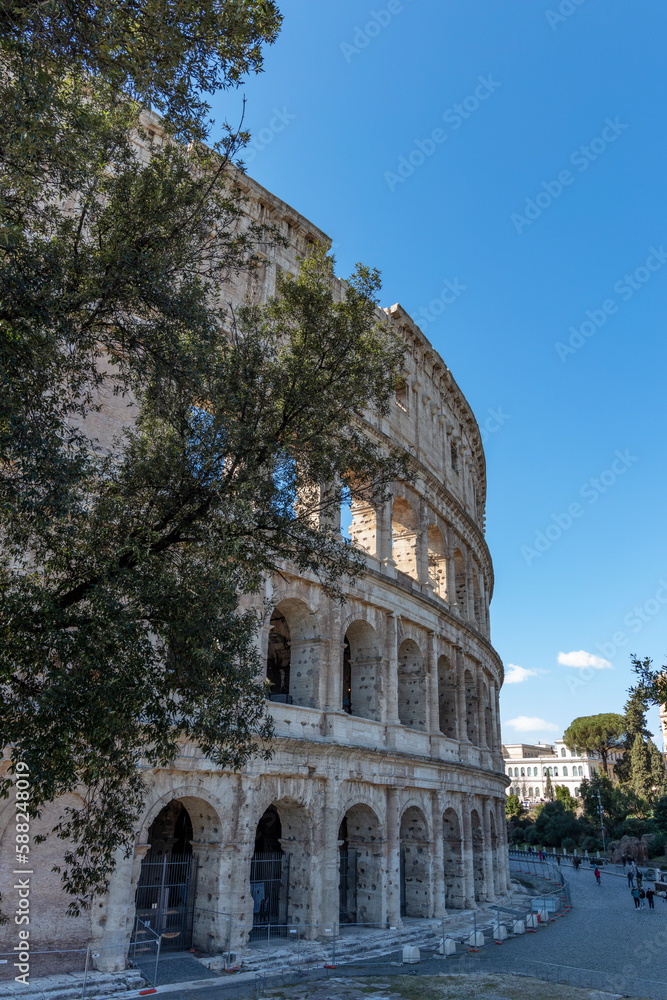 Fototapeta premium Glimpse of ancient Colosseum in Rome on a sunny day. Roman amphitheater and sun in Italy