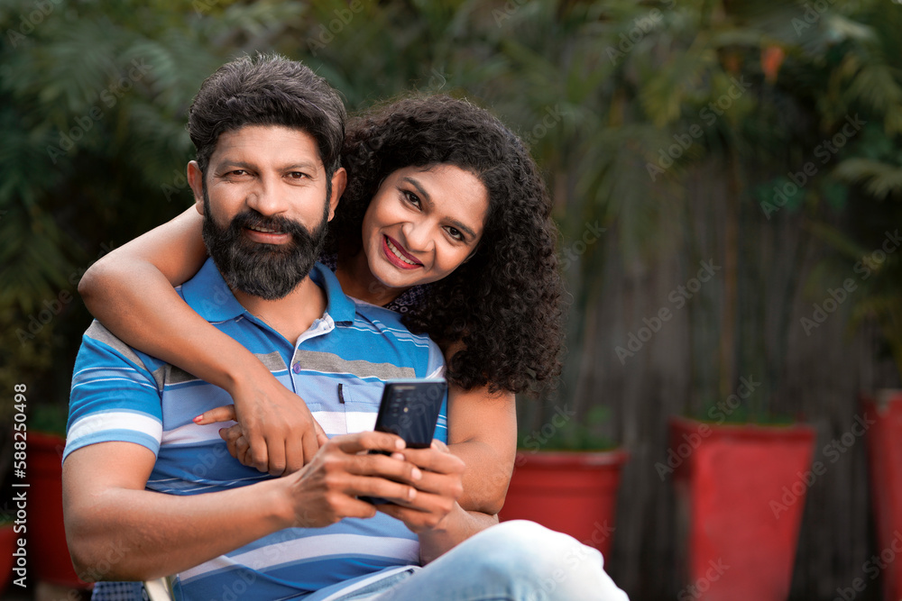 Happy indian couple sitting at out of home and using smartphone together. Happy indian couple sitting at out of home and using smartphone together.