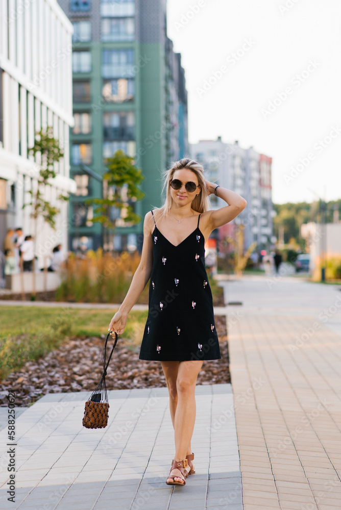 Beautiful happy blonde walks around the city in a black dress
