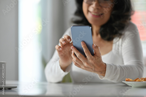 Carefree mature woman reading news online, checking social media on smart phone. Elderly technology concept