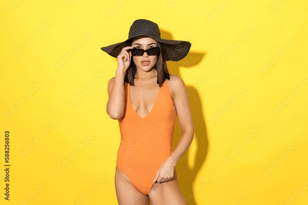 Summer is all about fun and relaxation, and this photo perfectly captures that vibe. A young woman in a swimsuit and summer hat looks radiant against the bright yellow background Summer is all about fun and relaxation, and this photo perfectly captures that vibe. A young woman in a swimsuit and summer hat looks radiant against the bright yellow background