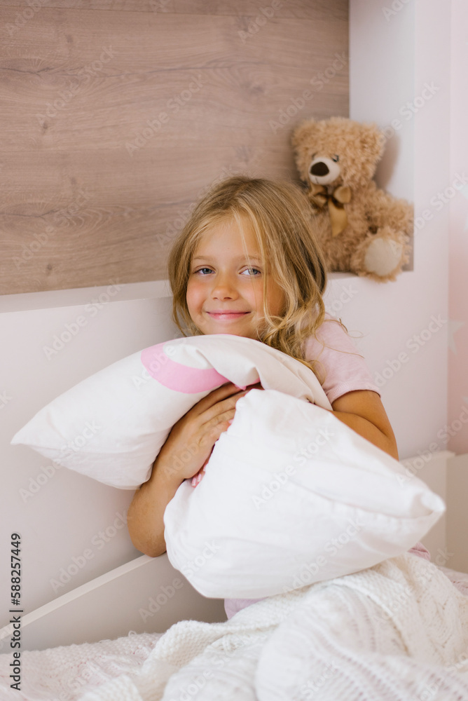 Happy contented girl child sitting on the bed hugging a pillow Happy contented girl child sitting on the bed hugging a pillow