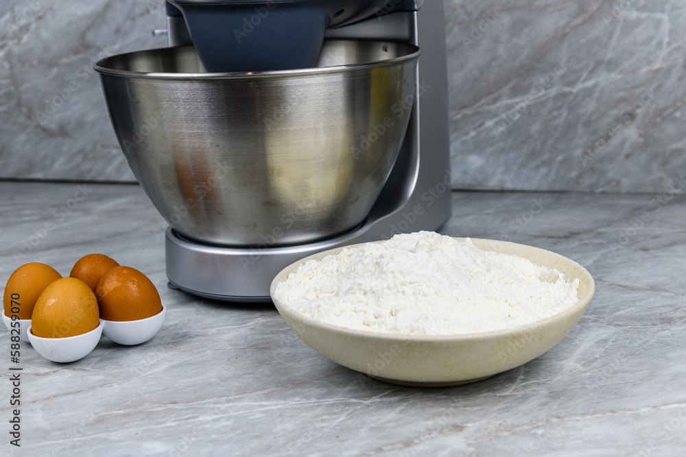 Fototapeta premium Modern food processor, eggs and plate with flour on a kitchen table