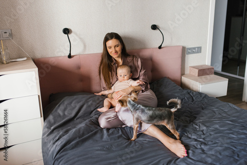 Mother with her baby song playing in the bed, playing with their dogs