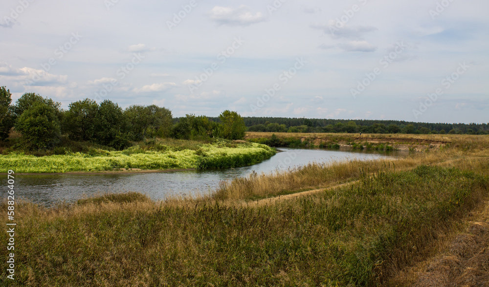 Beautiful landscape - the Klyazma river between the banks with green grass and trees against a cloudy sky on a summer day in the Moscow region and copy space
