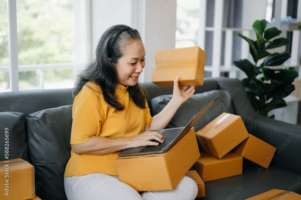 Senior business owner woman prepare parcel box and standing check online orders for deliver to customer on tablet, laptop Shopping Online concept.. Senior business owner woman prepare parcel box and standing check online orders for deliver to customer on tablet, laptop Shopping Online concept..