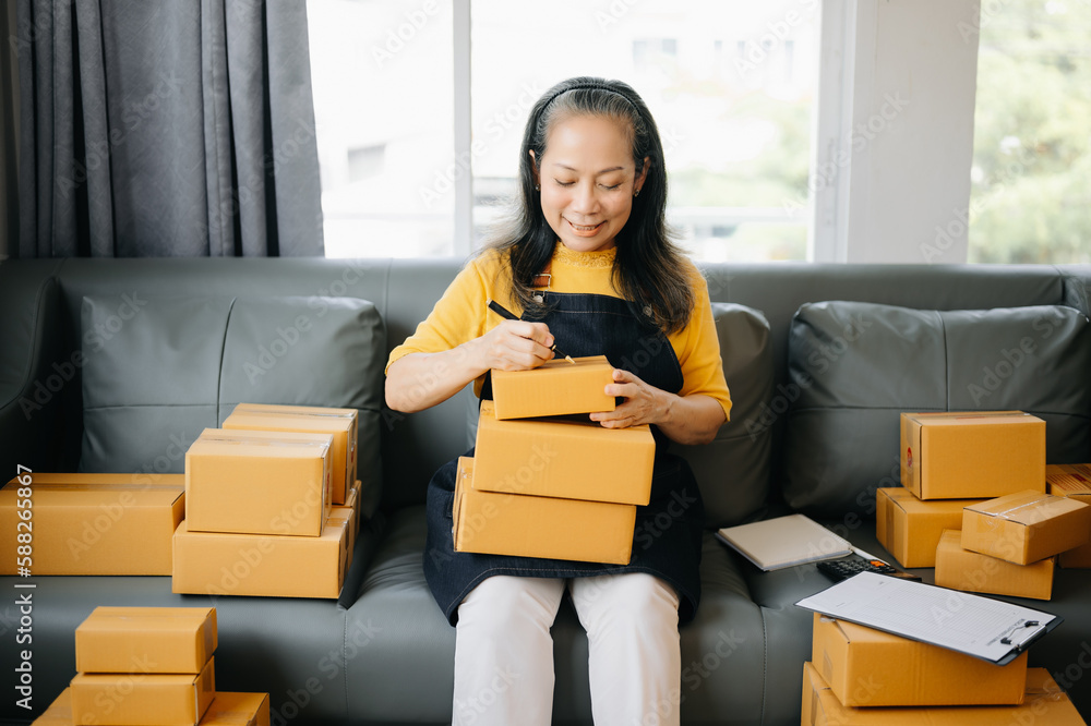 Startup small business SME, Entrepreneur owner Senior woman using smartphone or tablet taking receive and checking online purchase shopping order to preparing pack product box. Startup small business SME, Entrepreneur owner Senior woman using smartphone or tablet taking receive and checking online purchase shopping order to preparing pack product box.