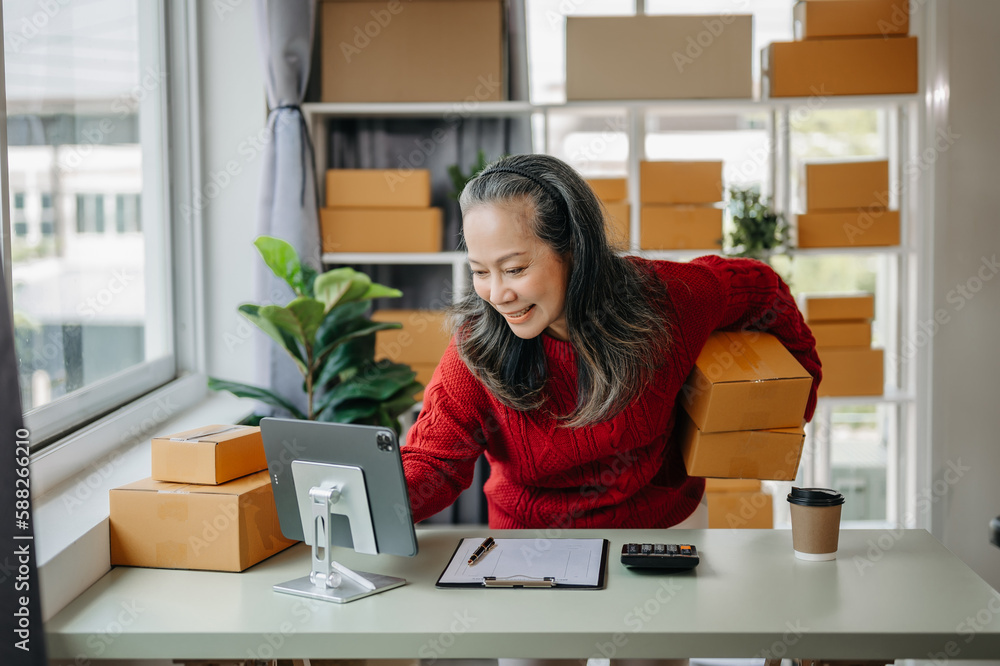 Senior business owner woman prepare parcel box and standing check online orders for deliver to customer on tablet, laptop Shopping Online concept. at home office. Senior business owner woman prepare parcel box and standing check online orders for deliver to customer on tablet, laptop Shopping Online concept. at home office.