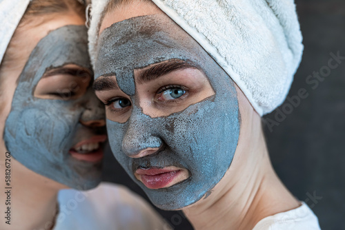 Two beautiful girls applying clay black mask isolated on black. Home take care of face skin
