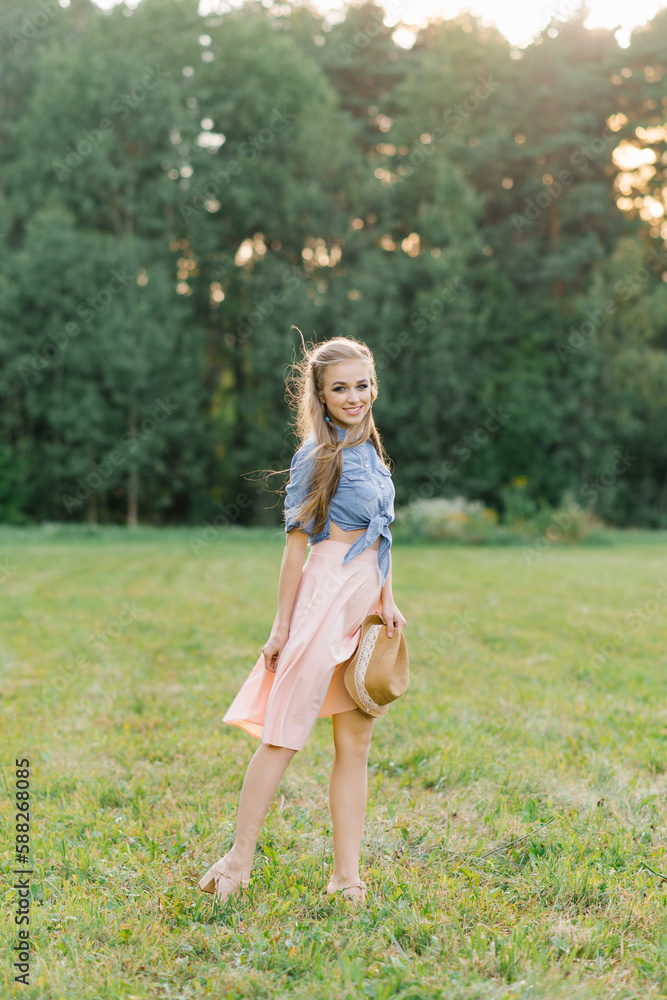 Happy Caucasian young woman, girl walking in the summer outdoors in nature, holding a hat in her hands Happy Caucasian young woman, girl walking in the summer outdoors in nature, holding a hat in her hands