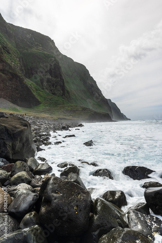 Rocky beach on Madeira Island, green volcanic cliffs at moody weather