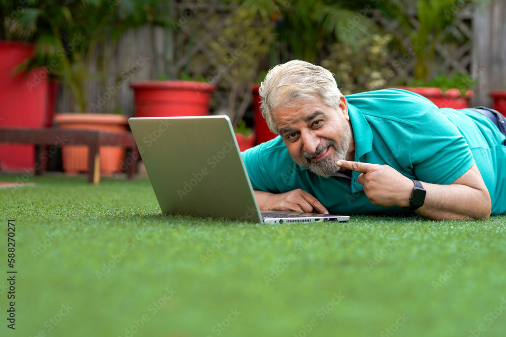 Indian senior man laying down at ground and using laptop. Indian senior man laying down at ground and using laptop.
