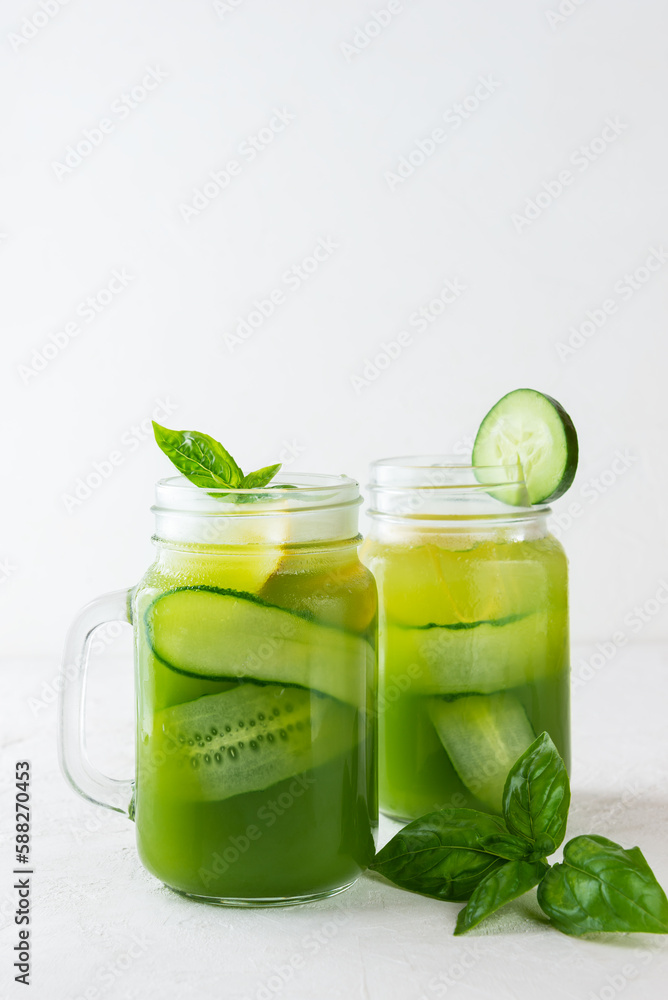 Fresh cucumber water with basil and lemon in a glass mug on light background. Fresh cucumber water with basil and lemon in a glass mug on light background.