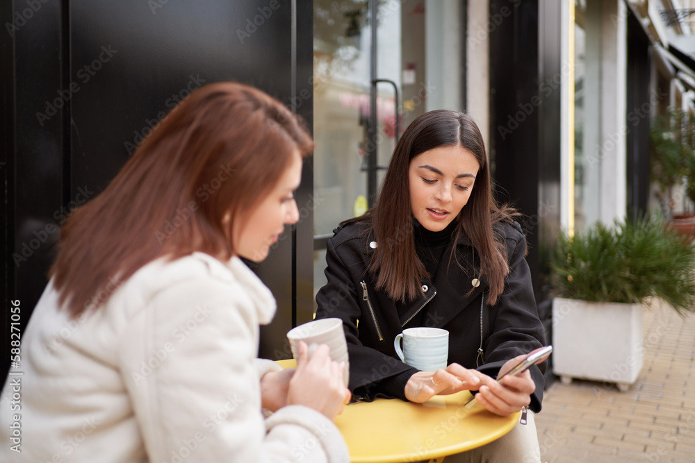 Two women using a mobile phone while drinking coffee at coffee shop. Technology and friendship concept. Two women using a mobile phone while drinking coffee at coffee shop. Technology and friendship concept.