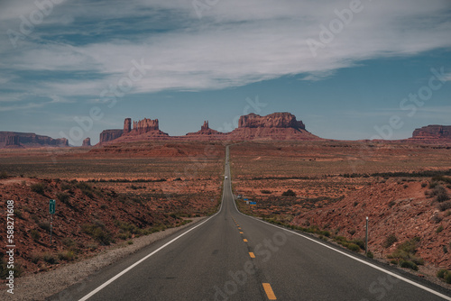 View of Monument Valley from Forrest Gump Point Mexican Hat, US-163 with street leading towards monuments. Blue sky and sunny day.