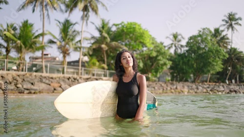 African american woman standing with surfboard in ocean water. Black female surfer posing with surf board. Pretty multiethnic girl goes from surfing session on tropical location. Extreme sports.