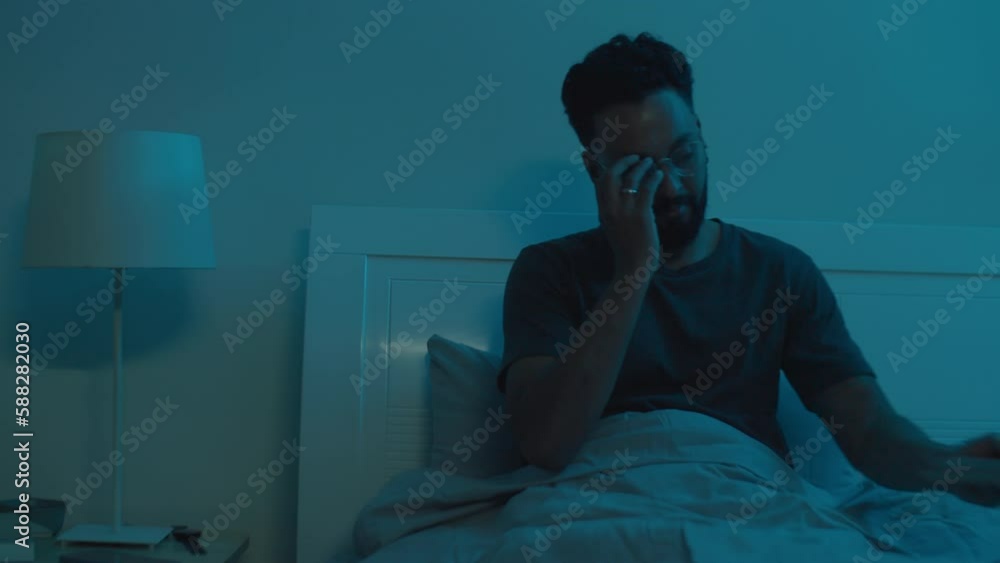 Medium shot of young bearded man using digital tablet, then putting it away, lying in bed and falling asleep in evening at home Medium shot of young bearded man using digital tablet, then putting it away, lying in bed and falling asleep in evening at home