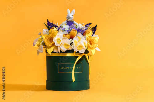 Easter decoration with beautiful spring flowers in box, Easter eggs and bunny on yellow background. Festive concept with copy space.