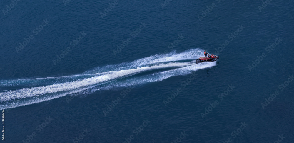 Naklejka premium The jet ski travels at great speed through blue water, leaving a foamy trail. View from above