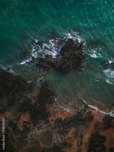 Aerial view of soft ocean waves splashing over the rocks on the beach