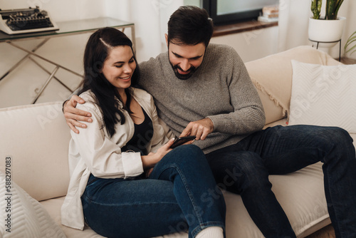 Cheerful couple using smartphone while sitting on couch