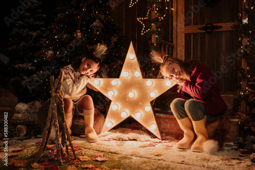 Girls leaning head on illuminated start shape light at Christmas