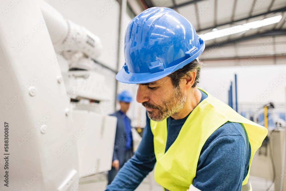 Engineer wearing hardhat working on robotic arm Engineer wearing hardhat working on robotic arm