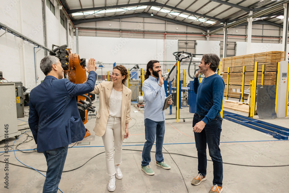 © Westend61 - Happy engineers giving high-five to each other in robotic industry