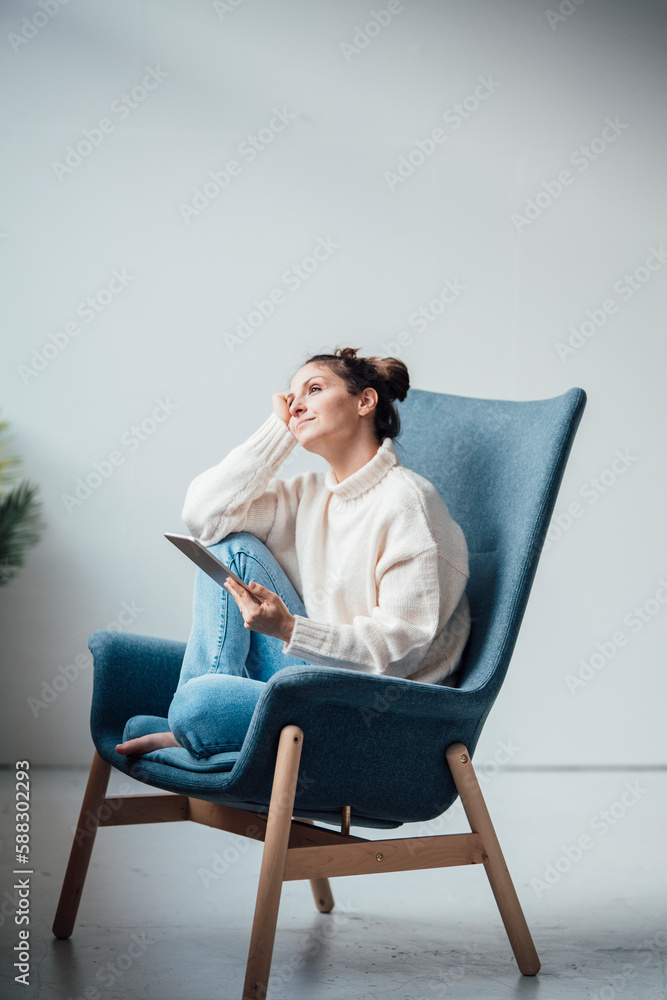 Thoughtful freelancer sitting with tablet PC in armchair at home Thoughtful freelancer sitting with tablet PC in armchair at home
