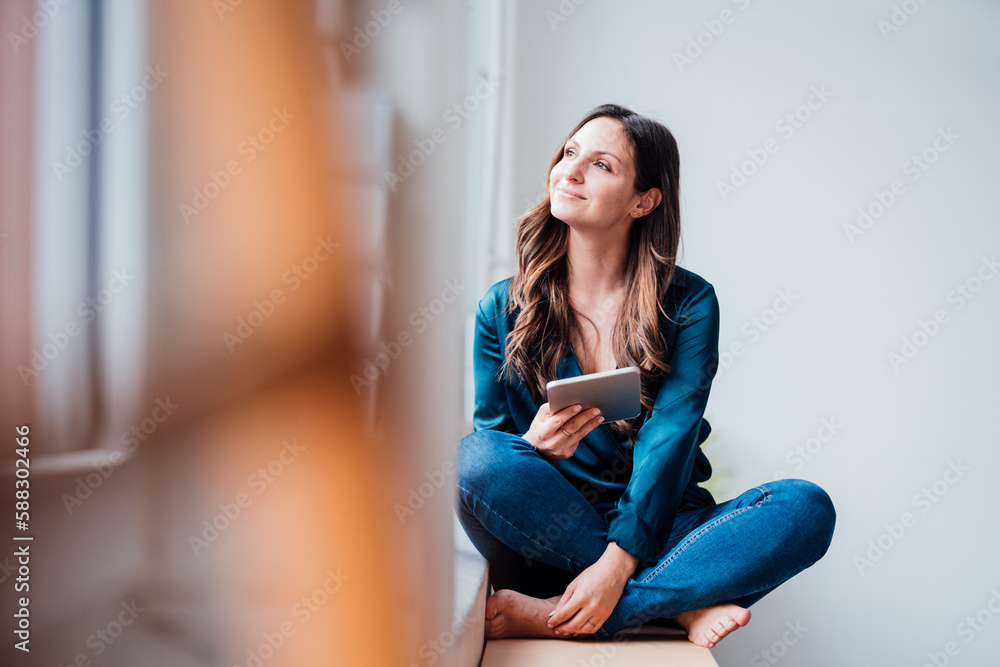 Smiling thoughtful freelancer sitting with tablet PC at home office Smiling thoughtful freelancer sitting with tablet PC at home office