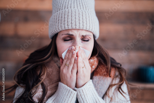 Sick woman wearing knit hat blowing nose