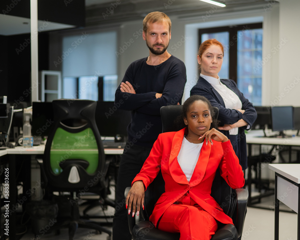 Caucasian red-haired woman, bearded Caucasian man stand behind a seated African American young woman in the office. Caucasian red-haired woman, bearded Caucasian man stand behind a seated African American young woman in the office.